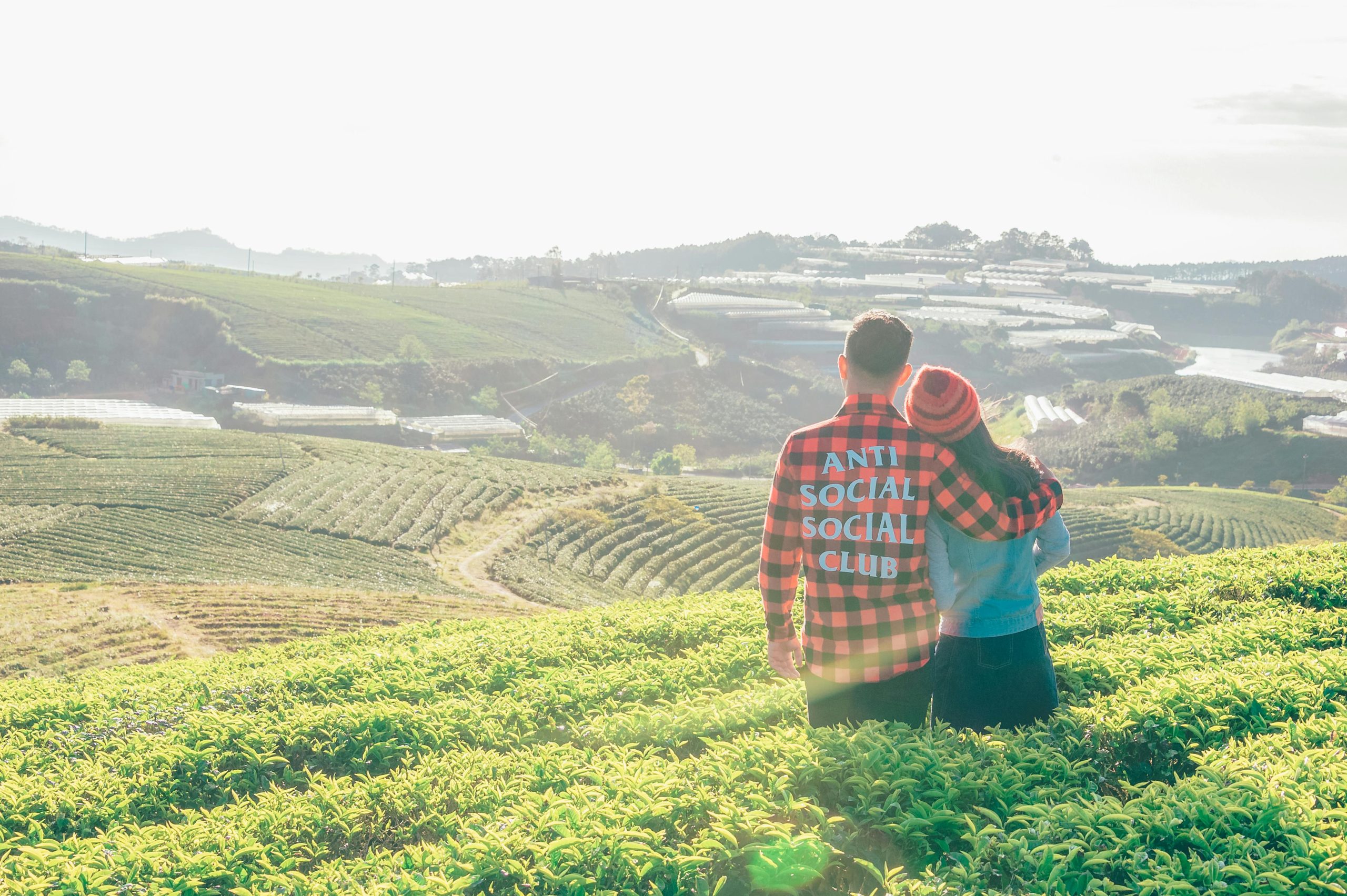 A couple embraces while viewing rolling green farmland under a clear sky.