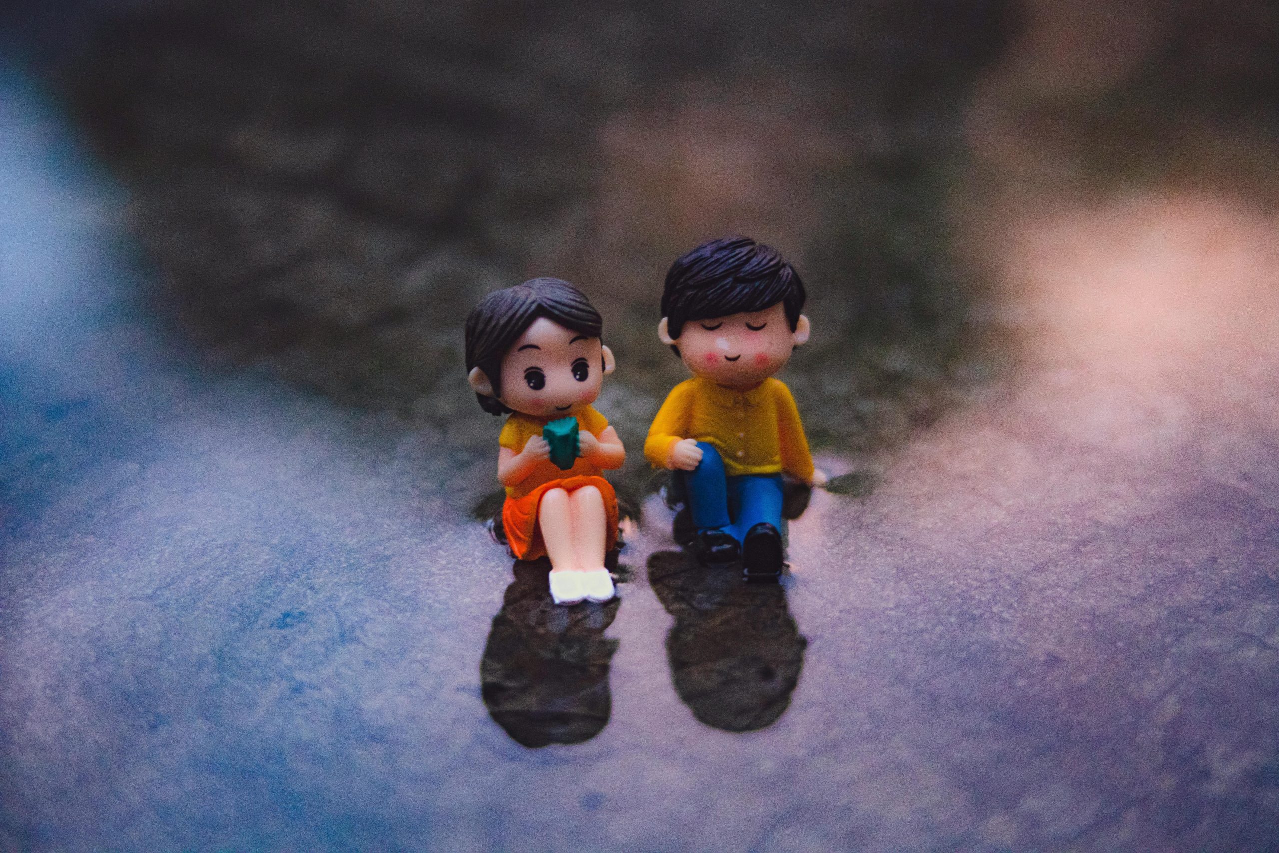 Cute miniature couple figurines sitting on a dreamy surface, evoking romance and artistic creativity.